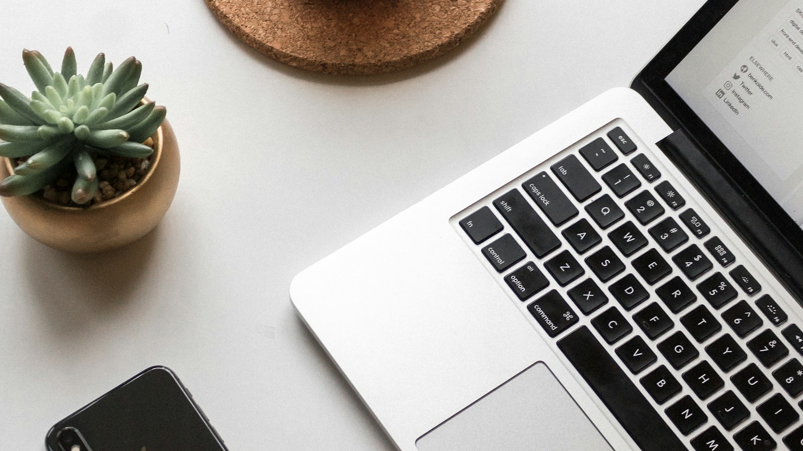 A laptop, a phone, and a succulent arranged on a white desk